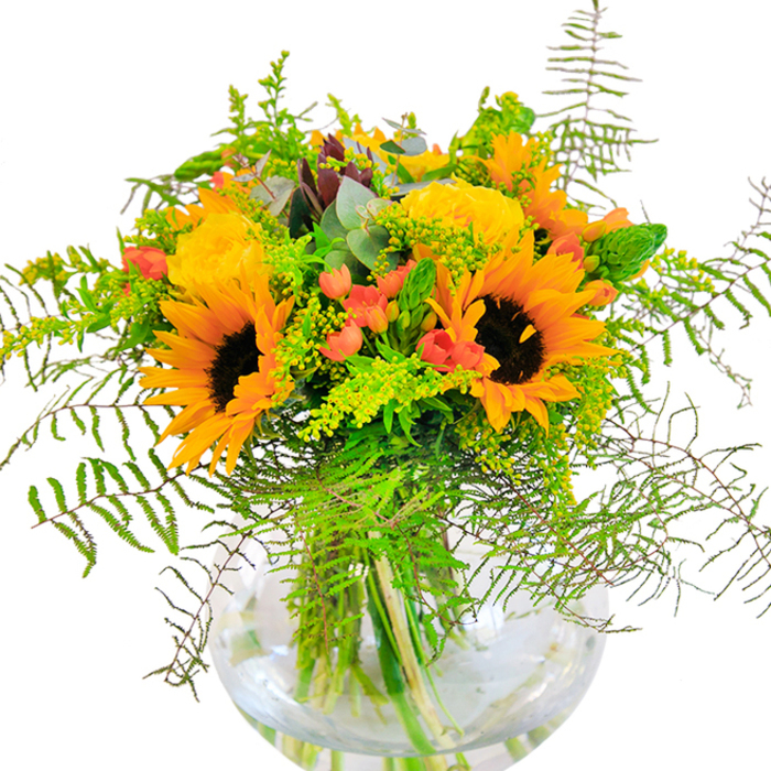 Immediately striking in both colour and composition, this bouquet is a joyful expression of seasonal abundance, drawing inspiration from Creekmouth's riverside scenery and open local spaces. The arrangement is anchored by a cluster of cheerful sunflowers, their bright, sunlit petals and rich chocolate-brown centers radiating positivity. Nestled beside them are plush yellow garden roses, each rosette a finely arranged spiral of soft, layered petals that imbue the bouquet with a sense of timeless refinement. Crimson hypericum berries peep out from within the greenery, their glossy skin and clustered form reminiscent of foraged finds in the parks near the Thames. The design is generously filled with cascading feathery ferns, airy goldenrod sporting petite yellow flowers, and slender bright green spikes, all harmonized by the addition of subtly aromatic, blue-green eucalyptus. The contemporary, clear glass vase-rounded like a droplet of water-provides a clean and modern anchor, revealing the stems' natural tangle within. Bathed in gentle daylight, the bouquet's swirling colours and intricate textures come to life, offering a feast for both eyes and senses. Crafted by the skilled hands of Creekmouth Flowers, this arrangement perfectly complements family celebrations, milestone events, or daily moments when a touch of joy is needed. Its freshness and radiant spirit make it a true reflection of Creekmouth's friendly, diverse charm.