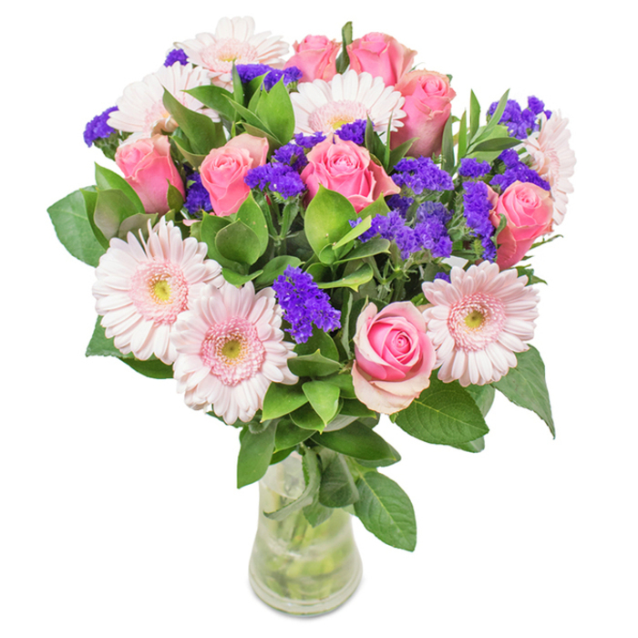 An eye-catching, gracefully arranged floral bouquet stands in a clear glass vase, poised against a crisp white background-its character reflecting Creekmouth's bright spirit near Barking Creek. Central to the display are approximately seven to nine pink roses, some unfurling, others in tight rosebud form, each revealing their classic spiral structure. They're gracefully joined by five to seven pale pink Gerbera daisies, with their large, round heads and creamy-white centers, all enhanced by clusters of brilliant purple statice weaving through the arrangement. The deep green foliage recalls the leafy riverbanks and waterside grasses of Creekmouth, providing a fresh, abundant base for the vibrant blooms above. The vase holds visible water and stems, suggesting freshness and the promise of swift local delivery from Creekmouth Flowers. This artful arrangement-roses, Gerberas, and purple fillers-fits perfectly for birthdays, anniversaries, or simply brightening local homes or offices, radiating joy and heartfelt feeling with every bloom.